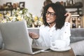 Young African American girl in glasses sitting in restaurant with laptop. Pretty girl with earphones joyfully looking in Royalty Free Stock Photo
