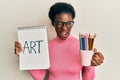 Young african american girl holding art notebook and colored pencils winking looking at the camera with sexy expression, cheerful Royalty Free Stock Photo