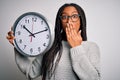 Young african american girl holding big minute clock over isolated background cover mouth with hand shocked with shame for Royalty Free Stock Photo