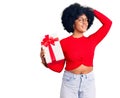 Young african american girl holding gift smiling confident touching hair with hand up gesture, posing attractive and fashionable Royalty Free Stock Photo