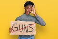 Young african american girl holding no guns warning banner smiling happy doing ok sign with hand on eye looking through fingers