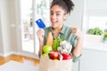 Young african american girl holding paper bag of groceries and credit card as payment very happy pointing with hand and finger Royalty Free Stock Photo