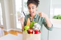 Young african american girl holding paper bag of groceries and credit card as payment very happy pointing with hand and finger Royalty Free Stock Photo