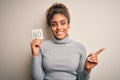 Young african american girl holding reminder paper with no word negative message very happy pointing with hand and finger to the