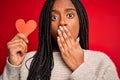 Young african american girl holding romantic heart paper shape over red isolated background cover mouth with hand shocked with Royalty Free Stock Photo