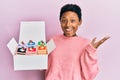 Young african american girl holding sweet pastries in a box celebrating achievement with happy smile and winner expression with Royalty Free Stock Photo