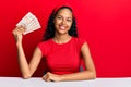 Young african american girl holding united kingdom pounds sitting on the table looking positive and happy standing and smiling