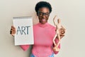 Young african american girl holding wooden manikin and art word on notebook smiling and laughing hard out loud because funny crazy Royalty Free Stock Photo