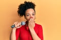 Young african american girl singing song using microphone and headphones covering mouth with hand, shocked and afraid for mistake Royalty Free Stock Photo