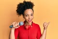 Young african american girl singing song using microphone and headphones pointing thumb up to the side smiling happy with open Royalty Free Stock Photo