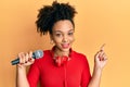 Young african american girl singing song using microphone and headphones smiling happy pointing with hand and finger to the side Royalty Free Stock Photo