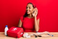 Young african american girl sitting on the table with first aid kit making cure smiling with hand over ear listening and hearing Royalty Free Stock Photo