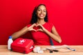 Young african american girl sitting on the table with first aid kit making cure smiling in love doing heart symbol shape with Royalty Free Stock Photo