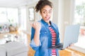 Young african american girl standing working using laptop pointing and showing with thumb up to the side with happy face smiling Royalty Free Stock Photo