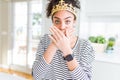 Young african american girl wearing golden queen crown on head shocked covering mouth with hands for mistake Royalty Free Stock Photo