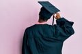 Young african american girl wearing graduation cap and ceremony robe backwards thinking about doubt with hand on head Royalty Free Stock Photo