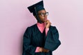 Young african american girl wearing graduation cap and ceremony robe with hand on chin thinking about question, pensive expression Royalty Free Stock Photo