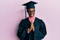 Young african american girl wearing graduation cap and ceremony robe praying with hands together asking for forgiveness smiling