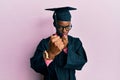 Young african american girl wearing graduation cap and ceremony robe ready to fight with fist defense gesture, angry and upset