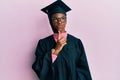 Young african american girl wearing graduation cap and ceremony robe thinking concentrated about doubt with finger on chin and Royalty Free Stock Photo