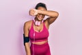 Young african american girl wearing gym clothes and using headphones covering eyes with arm smiling cheerful and funny Royalty Free Stock Photo