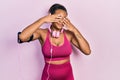 Young african american girl wearing gym clothes and using headphones covering eyes with hands smiling cheerful and funny Royalty Free Stock Photo