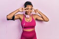 Young african american girl wearing gym clothes and using headphones doing peace symbol with fingers over face, smiling cheerful Royalty Free Stock Photo