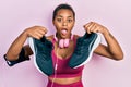 Young african american girl wearing gym clothes, using headphones and holding sporty shoes afraid and shocked with surprise and Royalty Free Stock Photo