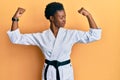 Young african american girl wearing karate kimono and black belt showing arms muscles smiling proud Royalty Free Stock Photo