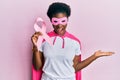 Young african american girl wearing superhero costume holding pink cancer ribbon celebrating victory with happy smile and winner