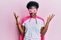 Young african american girl wearing superhero mask and cape costume celebrating mad and crazy for success with arms raised and