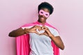 Young african american girl wearing superhero mask and cape costume smiling in love doing heart symbol shape with hands Royalty Free Stock Photo