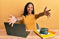 Young african american girl working at the office with laptop and calculator looking at the camera smiling with open arms for hug Royalty Free Stock Photo