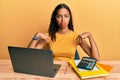 Young african american girl working at the office with laptop and calculator pointing down looking sad and upset, indicating