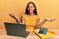 Young african american girl working at the office with laptop and calculator smiling cheerful with open arms as friendly welcome, Royalty Free Stock Photo