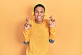 Young african american guy listening to music using headphones gesturing finger crossed smiling with hope and eyes closed Royalty Free Stock Photo