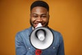 Young african american guy making annoucement with megaphone against yellow background