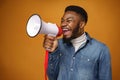 Young african american guy making annoucement with megaphone against yellow background