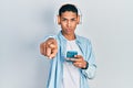 Young african american guy using smartphone wearing headphones pointing with finger to the camera and to you, confident gesture Royalty Free Stock Photo