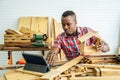 Young african american male carpenter sitting at table showing wooden items through tablet while video online chatting with
