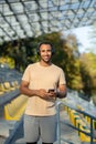 A young African-American male sportsman, athlete, runner in headphones stands in the stadium. Holds the phone in his Royalty Free Stock Photo