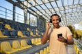 A young African-American male sportsman, athlete, runner in headphones stands in the stadium between the stands. Holds Royalty Free Stock Photo