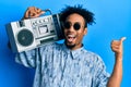 Young african american man with beard holding boombox, listening to music pointing thumb up to the side smiling happy with open Royalty Free Stock Photo