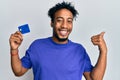 Young african american man with beard holding credit card pointing thumb up to the side smiling happy with open mouth Royalty Free Stock Photo