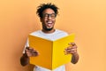 Young african american man with beard reading a book wearing glasses winking looking at the camera with sexy expression, cheerful Royalty Free Stock Photo