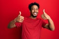 Young african american man with beard wearing casual red t shirt success sign doing positive gesture with hand, thumbs up smiling Royalty Free Stock Photo