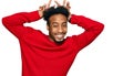 Young african american man with beard wearing casual winter sweater posing funny and crazy with fingers on head as bunny ears, Royalty Free Stock Photo
