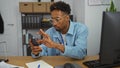 Young, african american man with a beard working on his smartphone in a modern office environment Royalty Free Stock Photo