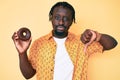 Young african american man with braids holding donut with angry face, negative sign showing dislike with thumbs down, rejection