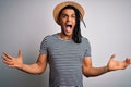Young african american man with dreadlocks on vacation wearing striped t-shirt and hat crazy and mad shouting and yelling with Royalty Free Stock Photo
